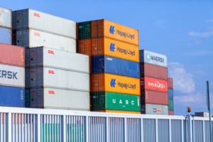 A STACK OF SHIPPING CONTAINERS BEARING VARIOUS LOGOS, INCLUDING MAERSK AND HAPAG-LLOYD