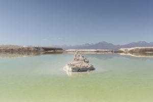 A ROCK STRUCTURE SITS IN THE MIDDLE OF A LARGE BRINE POOL AT A CHILEAN LITHIUM MINE.