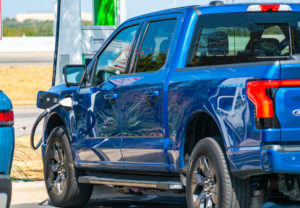 AN ELECTRIFIED BLUE FORD F-150 LIGHTNING PICKUP TRUCK IS PLUGGED INTO AN EV CHARGER.