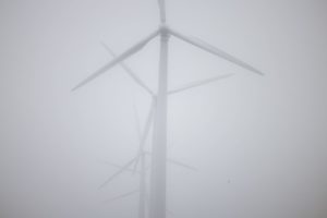 A LINE OF FOUR OFFSHORE WIND TURBINES ENGULFED IN FOG.