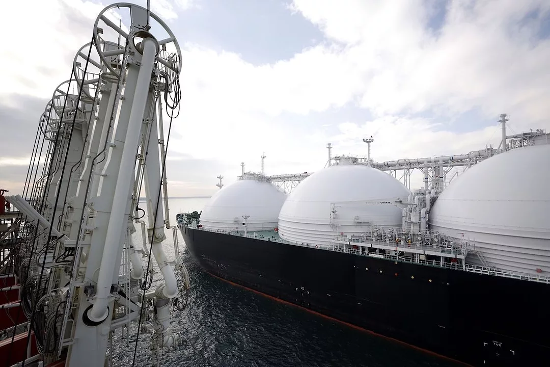 A LIQUIFIED NATURAL GAS TANKER IN A HARBOR NEXT TO INDUSTRIAL CRANES.