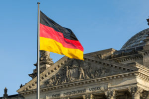 A GERMAN FLAG ON A FLAGPOLE WAVING IN FRON OF THE REICHSTAG BUILDING.
