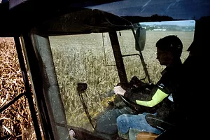 A FARM WORKER SITS IN THE CAB OF AN AGRICULTURAL VEHICLE SURROUNDED BY FIELDS OF GRAIN