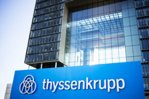 A THYSSENKRUPP SIGN CAN BE SEEN IN FRONT OF A LARGE GLASS BUILDING.