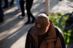 A WORKER IN A BROWN UPS HAT STARES AT THE GROUND.