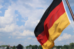 A GERMAN FLAG HANGING FROM A FLAG POLE FLAPS IN THE WIND IN FRONT OF A BLUE SKY.