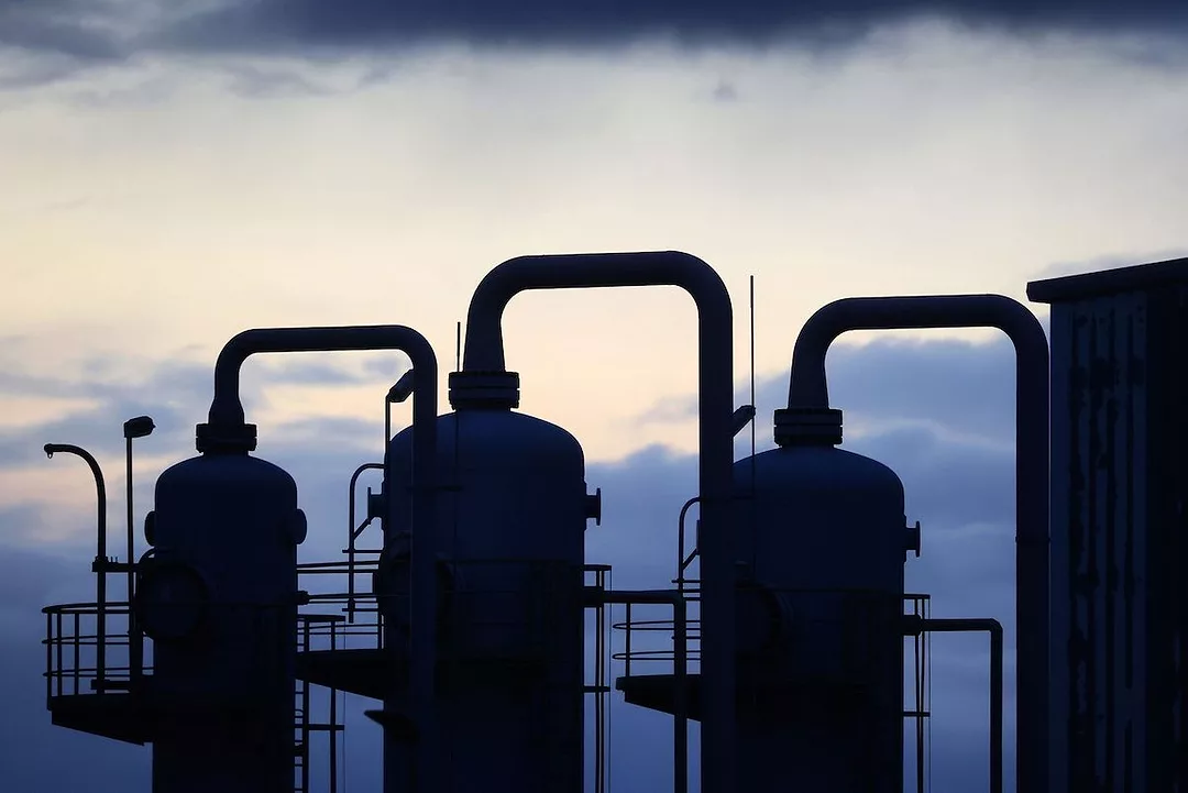 PIPES AND STORAGE UNITS AT A GAS STORAGE FACILITY UNDER A SETTING SUN.