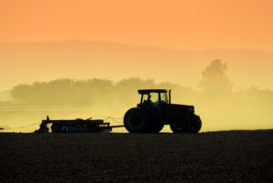 SILHOUETTE OF A TRACTOR RAKING SOIL AT SUNSET.