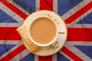 A CUP OF TEA AND A BISCUIT SIT ON TOP OF A SAUCER PLATE THAT IS PLACED ON TOP OF A UNION JACK FLAG.