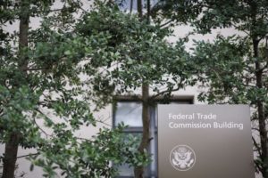 A FEDERAL TRADE COMMISSION SIGN IN FRONT OF THE FTC BUILDING UNDER TREES.