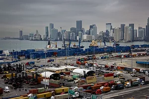 TRUCKS WAITING IN LINE AT A PORT UNDER A GREY SKY.