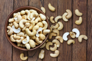 AERIAL VIEW OF A WOODEN BOWL OF CASHEWS AND SOME CASHEWS ON A DARK WOODEN TABLE.