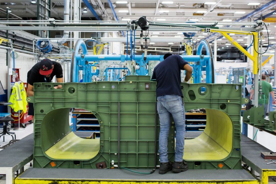 TWO WORKERS WORK ON A LARGE AIRLINE PART IN A FACTORY