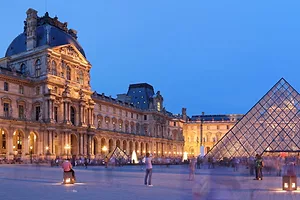A LARGE ROCOCO-STYLE BUILDING IS FRONTED BY A GLASS PYRAMID