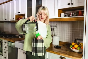 Young woman in a home kitchen pouring hot water into a hot water bottle.