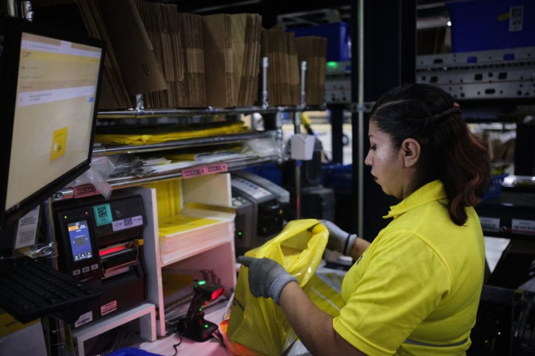 A WORKER IN A YELLOW SHIRT PACKS A YELLOW PLASTIC BAG AT A PICKING STATION IN A WAREHOUSE