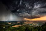 A BREATHTAKING IMAGE OF A HUGE DARK CLOUD FRONT SENDING RAIN AND LIGHTNING DOWN ONTO A RURAL AREA