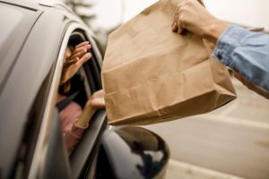 A BROWN PAPER BAG IS GIVEN TO SOMEONE THROUGH AN OPEN CAR WINDOW