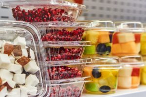 STACKS OF CLEAR PLASTIC CLAMSHELL PACKAGING HOLD CHOPPED COCONUT, POMEGRANATE SEEDS AND MELON.