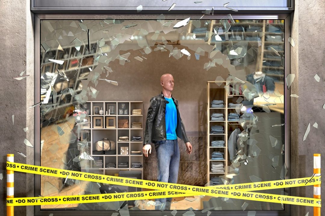 Destroyed boutique store shopfront showcase broken with pieces of glass, crime tape beside and mannequin behind