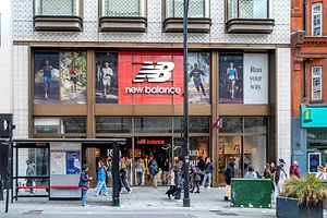 PEDESTRIANS WALK PAST THE ENTRANCE TO A NEW BALANCE STORE ON A BUSY CITY STREET
