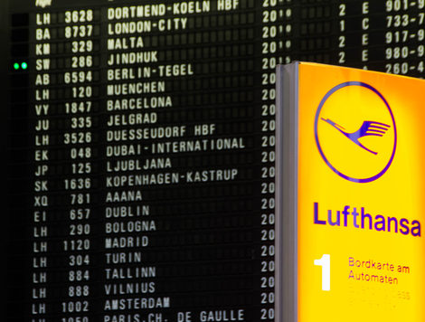 A Lufthansa sign in front of a list of flights in an airport