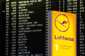 A Lufthansa sign in front of a list of flights in an airport