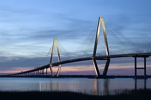 A LARGE, MODERN BRIDGE SPANS A CALM WATERWAY AT DUSK.