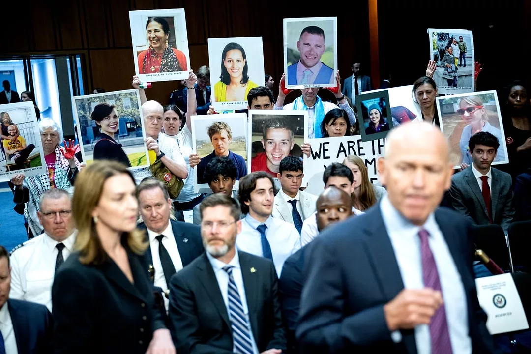 A BALDING MIDDLE AGED MAN IN A SUIT HURRIES PAST PEOPLE HOLDING PHOTOS OF RELATIVES