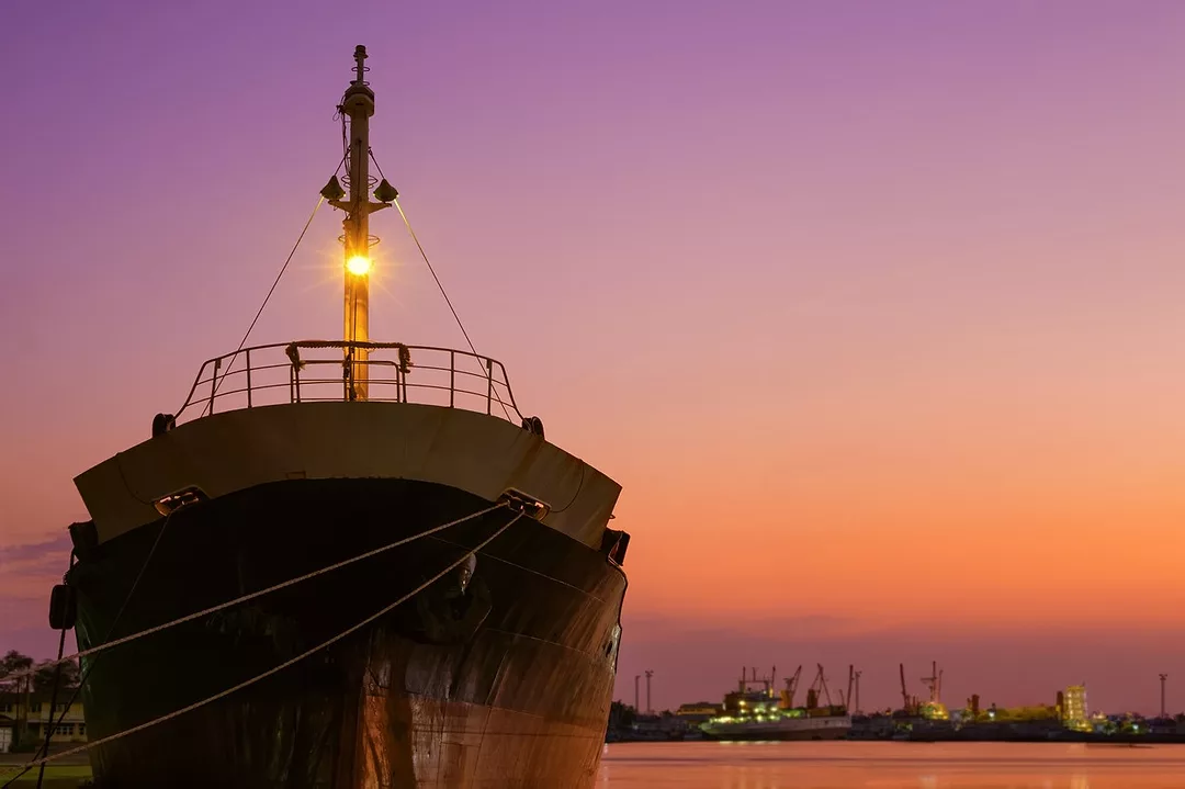 An old oil tanker ship is moored in shipyard area at harbor during renovation work against colorful pink twilight sky background