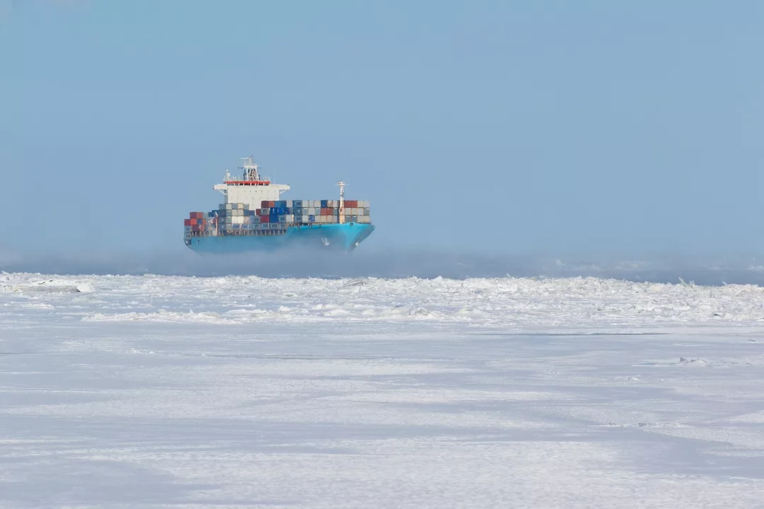 A cargo ship loaded with containers in the distance, moving through an icy, frozen sea