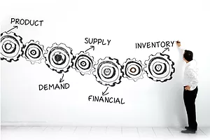 A MAN IN DARK PANTS AND A WHITE SHIRT PEERS AT A GIANT CHART SHOWING COGS REPRESENTING DIFFERENT STAGES OF BUSINESS PLANNING