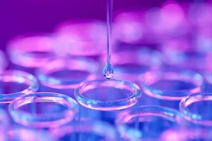 A DROP OF LIQUID FALLS INTO ONE OF A CLUSTER OF TEST TUBES