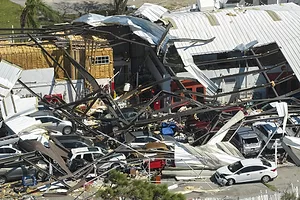 A group of cars buried under a warehouse damaged by a hurricane