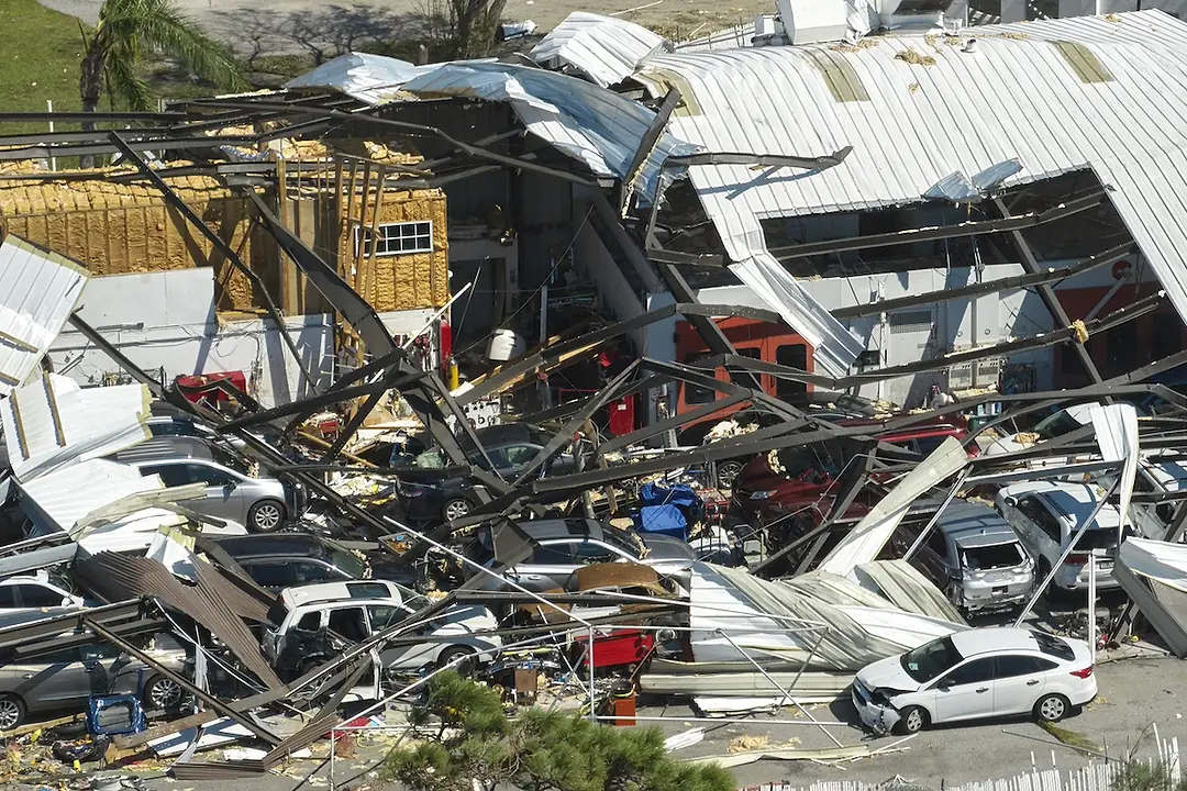 A group of cars buried under a warehouse damaged by a hurricane