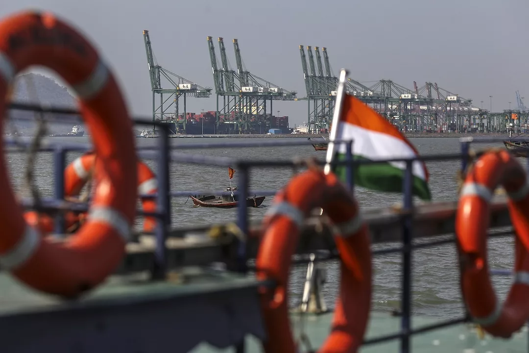 A wide view of three large cranes at a shipping port, with a row of orange life preservers along a rail in the foreground