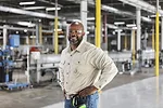 WORKER ASSEMBLY LINE FACTORY MANUFACTURING iStock-kali9-1366345325.jpg A SMILING MAN IN SAFETY GOGGLES STANDS, HANDS ON HIPS, IN FRONT OF A PRODUCTION LINE