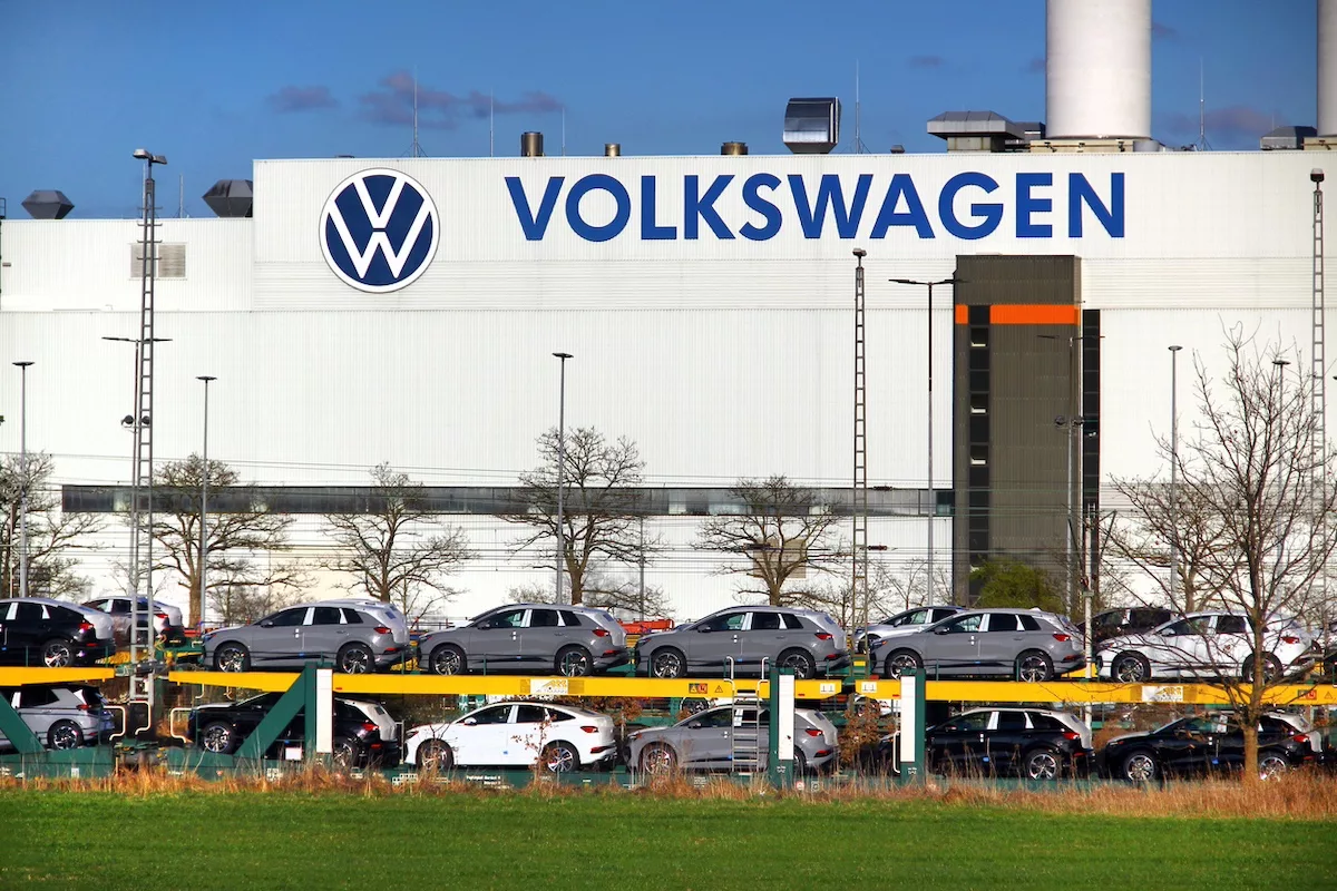 Volkswagen logolu büyük beyaz endüstriyel bina; önünde bir sıra park halinde otomobil