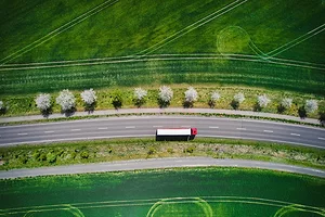 An overhead view of a white and red semi-truck driving on a rode alongside green grass fields