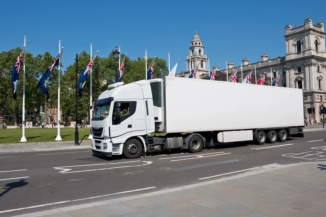 A white semi-truck pulling a white cab, along a road lined with British flags.
