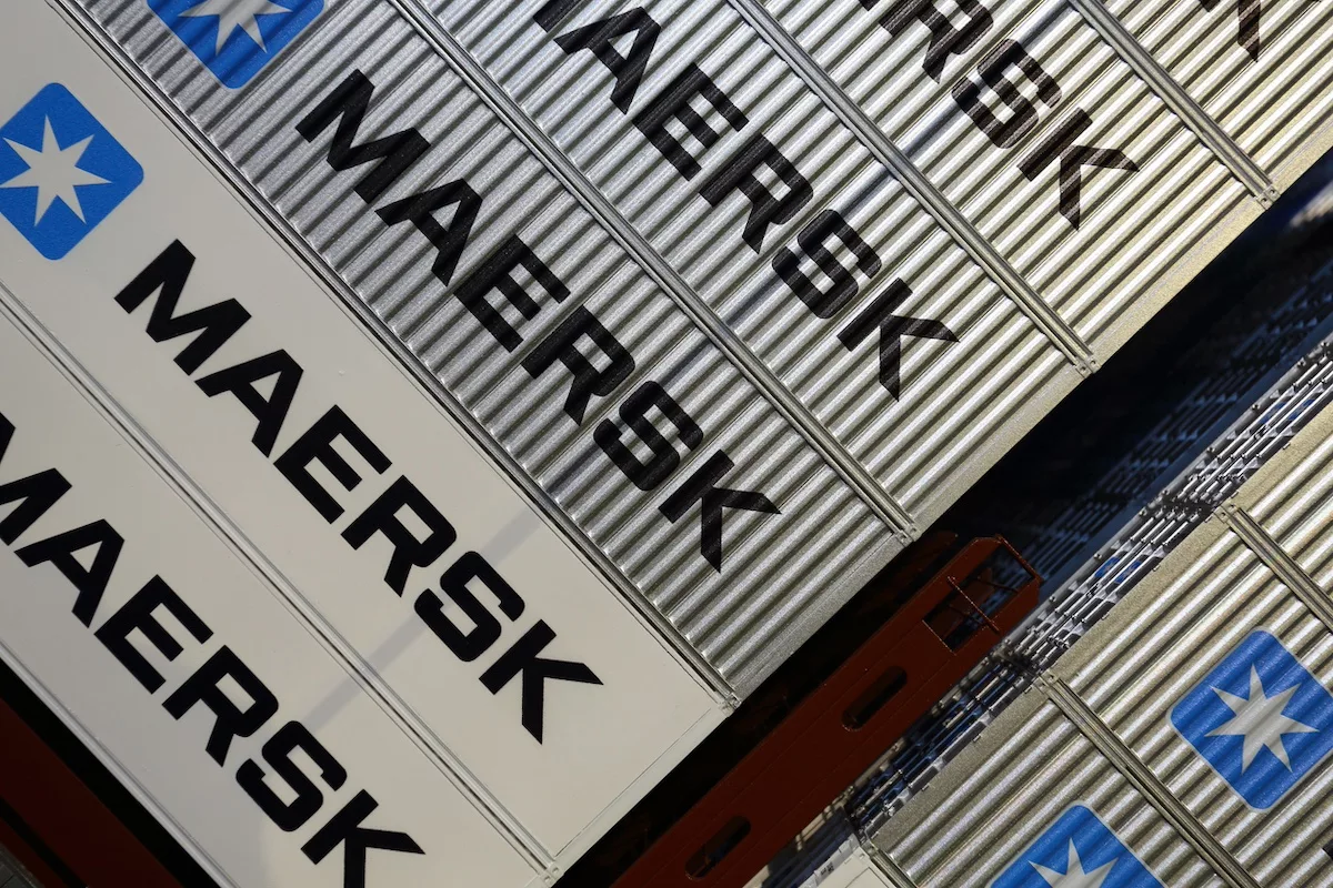 Üzerinde büyük siyah harflerle MAERSK yazan ve mavi yıldız logosu bulunan gri konteynerlerin havadan görünümü