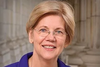 A WOMAN WITH SHORT BLONDE HAIR AND SPECTACLES SMILES INTO THE CAMERA