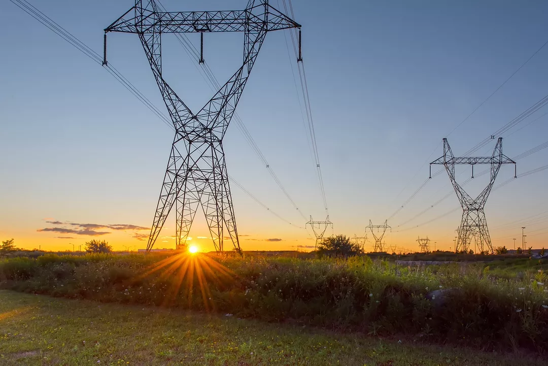 A row of tall power lines spread out across a green field at sunset