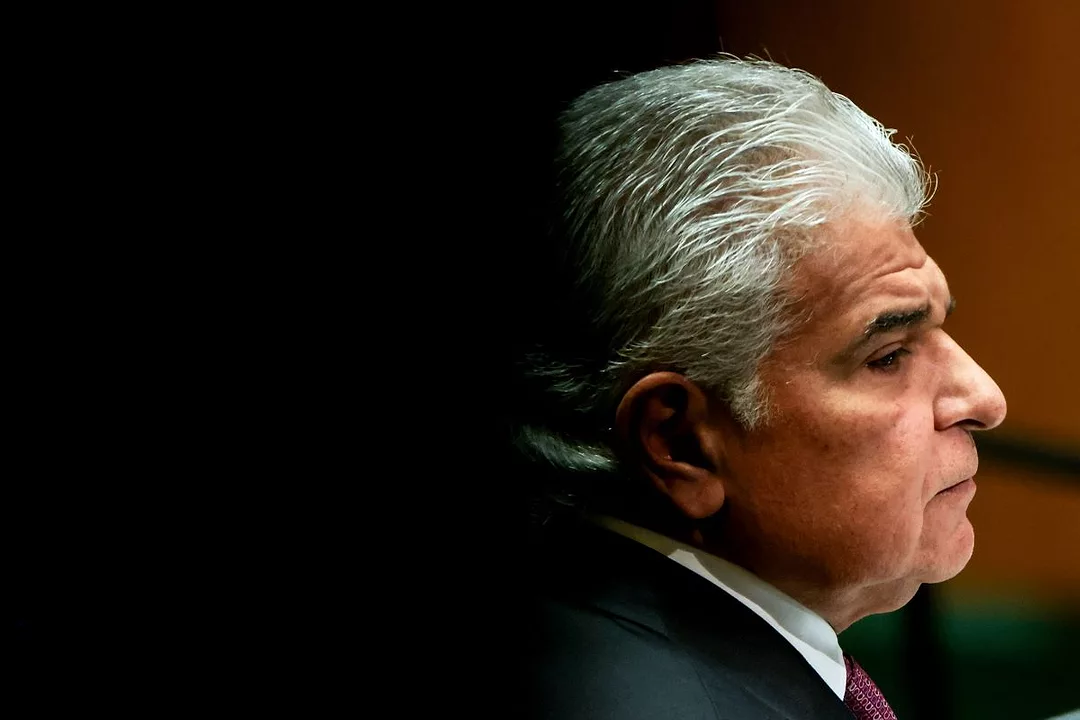 A GREY HAIRED MAN IN A JACKET, SHIRT AND TIE, IS SEEN FROM THE SIDE, HIS FACE RAISED TO THE LIGHT