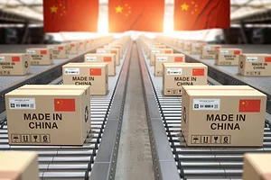 Rows of brown cardboard packages with "Made in China" written along each, moving along conveyer belts in front of three Chinese flags hanging from the rafters