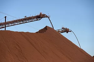 A large pile of brown sandy-looking material, with a pair of cranes towering over the pile in the background