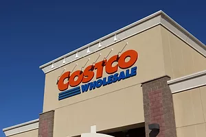 A tan storefront with two brick pillars flanking the entrance, with "Costco Wholesale" written in red and blue letters across the top