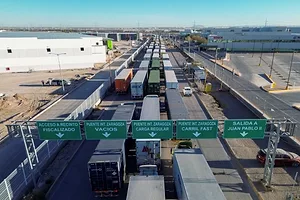 TRUCKS DRIVE DOWN A FIVE-LINE HIGHWAY UNDER GREEN AND WHITE SIGNS IN SPANISH