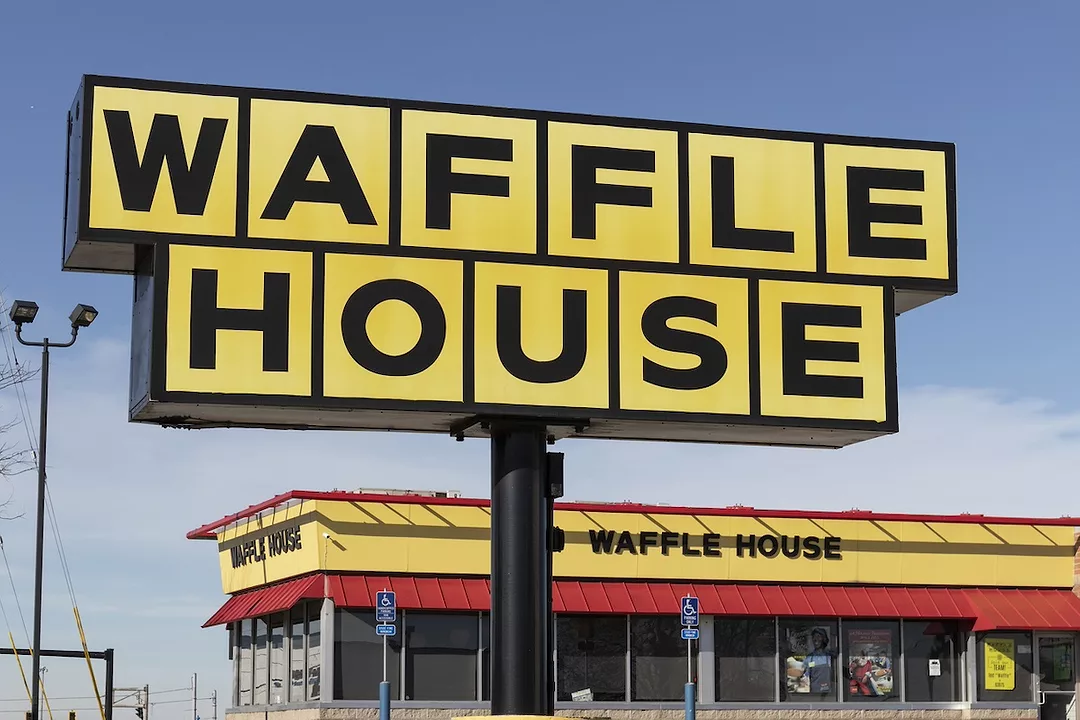 A large yellow sign that reads "WAFFLE HOUSE" outside of a yellow and red diner with the same black lettering across the top.