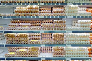 Five shelves in a grocery store dairy aisle filled with cartons of brown and white eggs